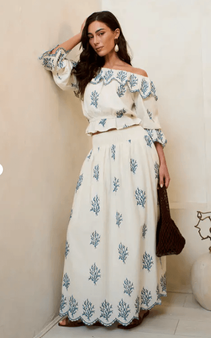 A woman wearing a teal cotton embroidered skater maxi skirt with intricate white bohemian embroidery, styled with a casual top.