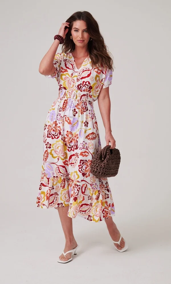 15 Stunning Trendy Summer Dresses Ideas To Elevate Your Style In 2026 10 A model wearing the Floral Printed Smocked Waist Midi Dress in ivory, orange, and lilac with a V-neckline and smocked waist, styled for sunny days.