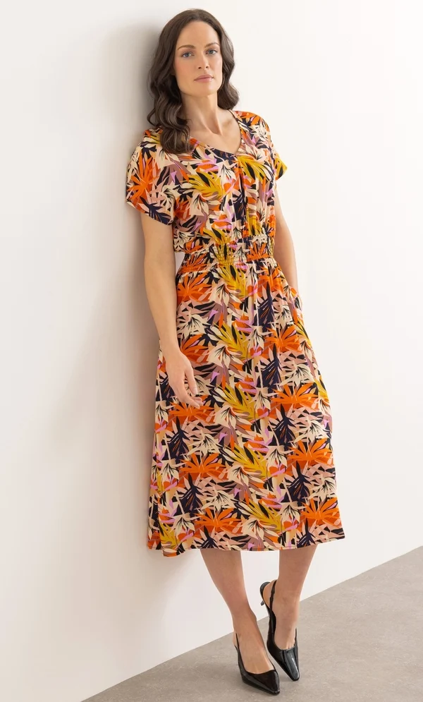 15 Stunning Trendy Summer Dresses Ideas To Elevate Your Style In 2026 16 A model wearing the Printed Smocked Waist Midi Dress in black and orange featuring a V-neckline, short sleeves, and a smocked waist for casual summer styling.