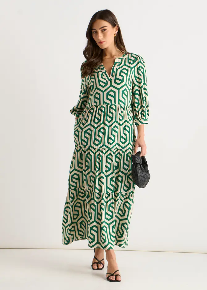 A stylish woman standing outdoors wearing the Gini London green geo print smock midi dress with long sleeves, showcasing chic smart-casual and casual fashion for urban settings.