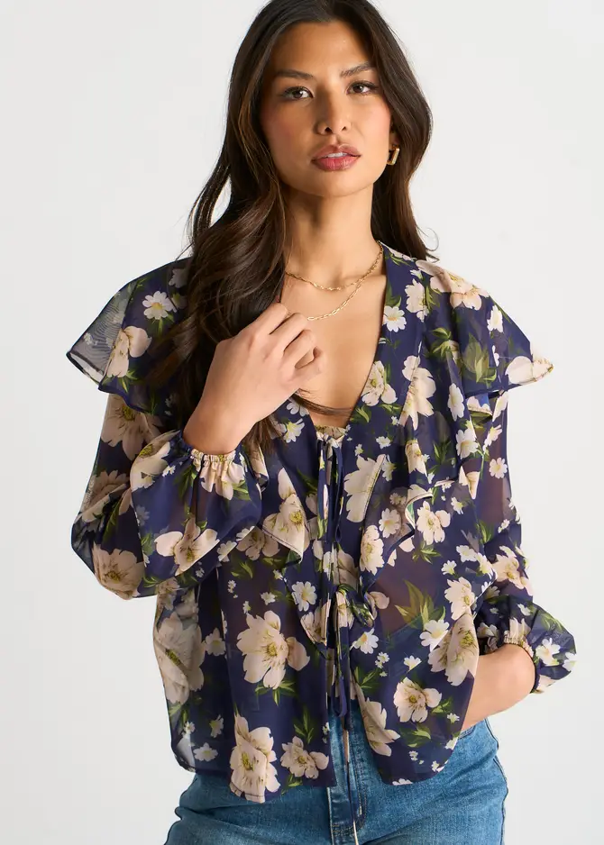 2026 Summer Wardrobe Capsule: Best Essential Pieces 21 A model wearing the Navy Elegant Floral Ruffle Shoulder Blouse featuring a floral print, long sleeves, and front ruffle details, styled as a chic staple for a spring capsule wardrobe 2026 women's outfit.